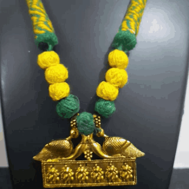 a necklace with yellow and green beads and a gold peacock pendant