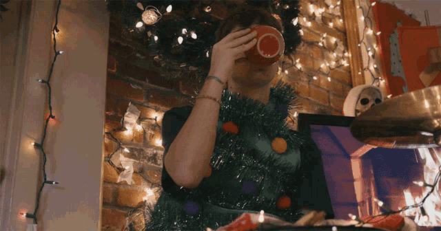 a man wearing a christmas tree sweater drinks from a cup