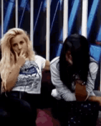 two women are sitting next to each other on a couch and one is covering her mouth with her hand .