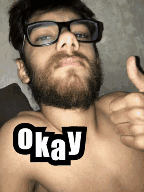 a shirtless man with glasses and a beard is giving a thumbs up with the word okay on his chest