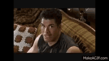 a man in a black tank top is sitting on a bed .