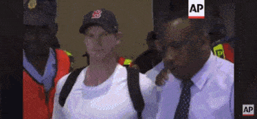 a man wearing a boston red sox hat is being escorted by a man in a suit