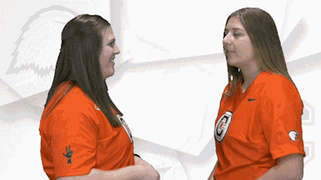 two women standing next to each other wearing orange shirts with the letter c on them