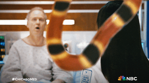a man in a hospital bed is talking to a snake with the nbc logo in the background