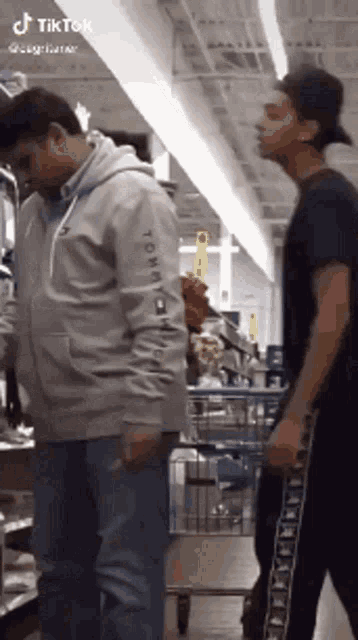 two men are standing next to each other in a store . one is wearing a tommy hilfiger hoodie .