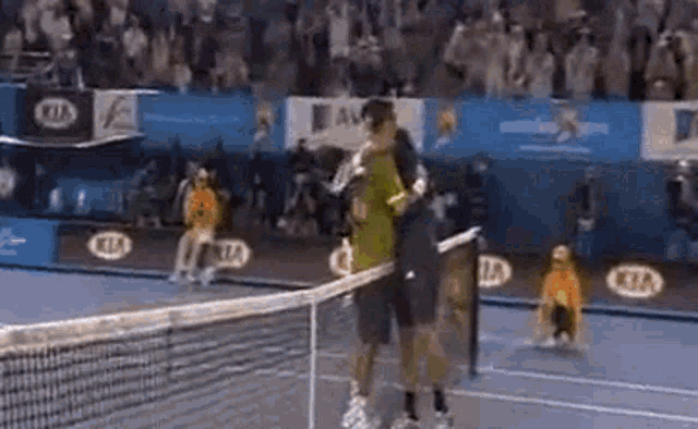 two men are hugging each other on a tennis court with kia advertisements on the wall behind them