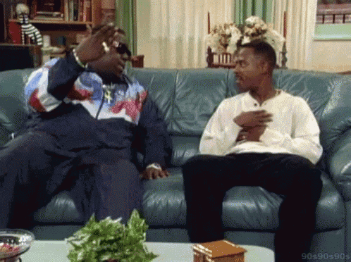 two men are sitting on a couch talking to each other in a living room .