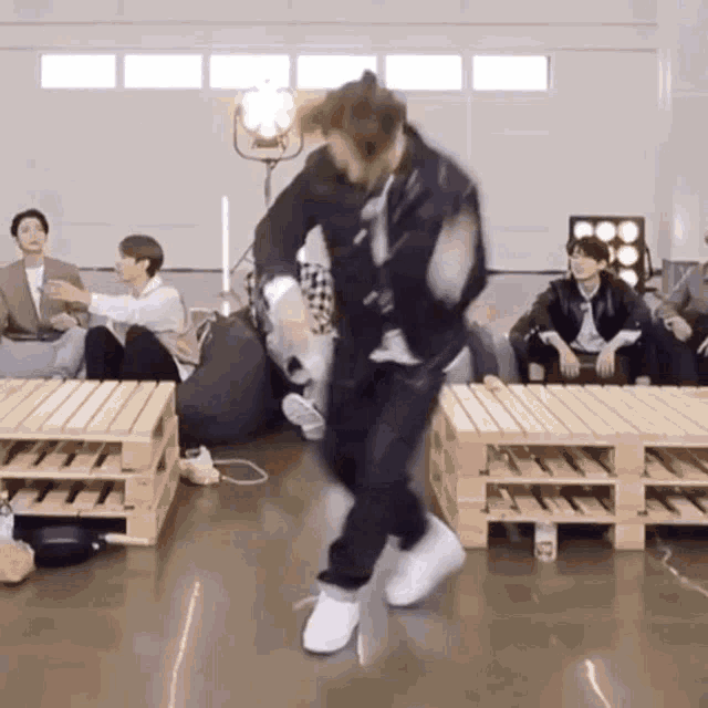 a man is dancing on a stage in front of a group of people sitting on wooden pallets .