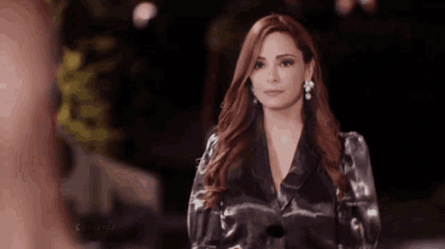 a woman with red hair is wearing a black jacket and silver earrings