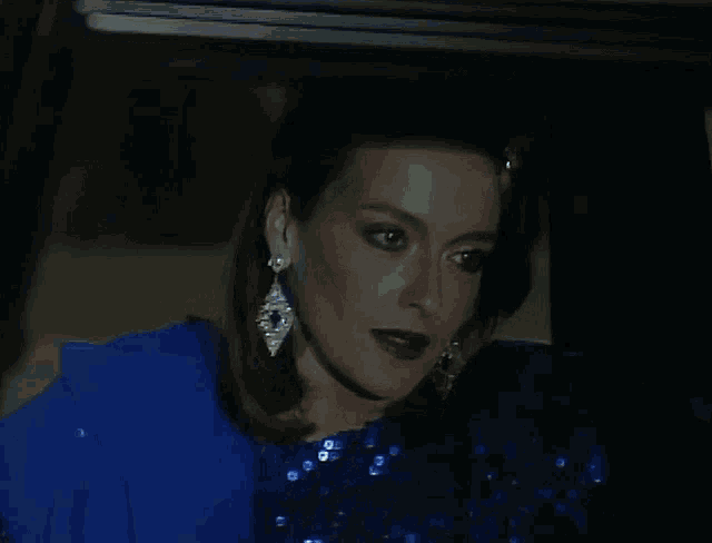 a woman wearing a blue sequined top and earrings looks at the camera