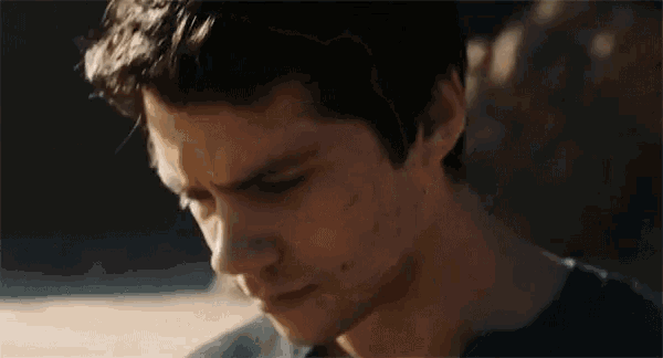a close up of a young man 's face looking at the camera with a rock in the background .
