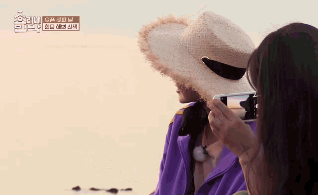 a woman taking a picture of a man wearing a straw hat and a purple jacket