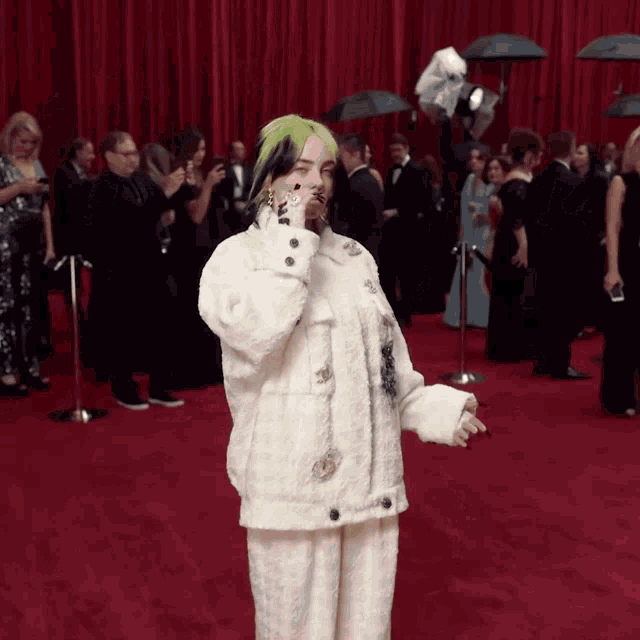 a woman with green hair is standing on a red carpet in front of a crowd