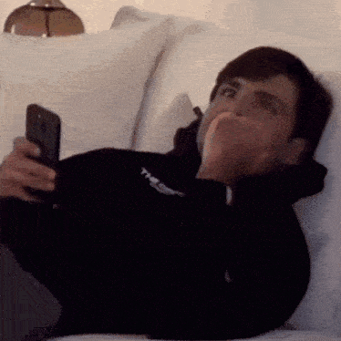 a man is laying on a couch holding a cell phone in his hand .