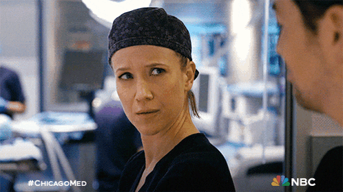 a woman wearing a scrub cap looks at a man in an operating room with the hashtag #chicagomed on the bottom left
