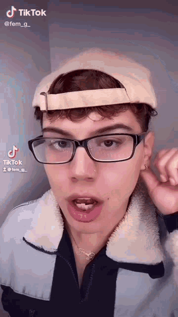 a young man wearing glasses and a hat is making a face .