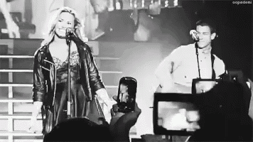 a woman singing into a microphone while a man takes a picture