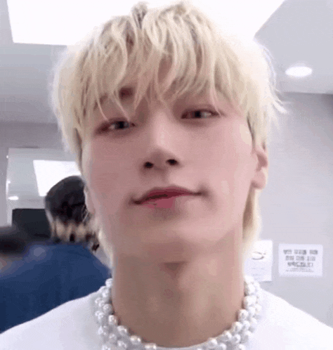 a close up of a young man wearing a pearl necklace and a white shirt .