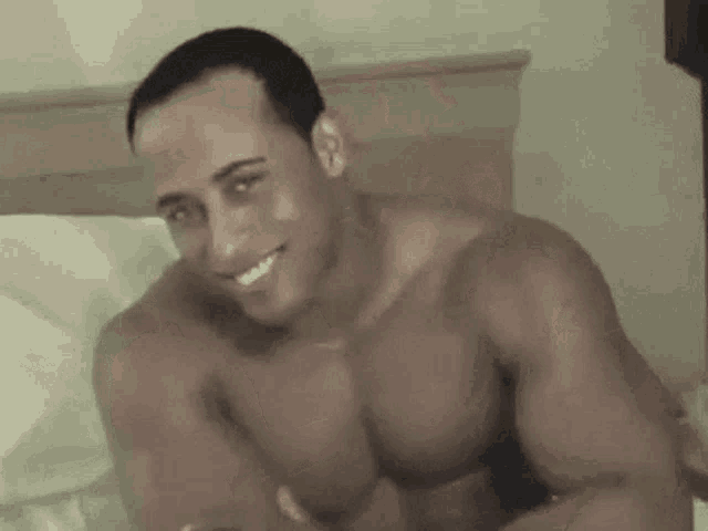 a shirtless man is laying on a bed and smiling .