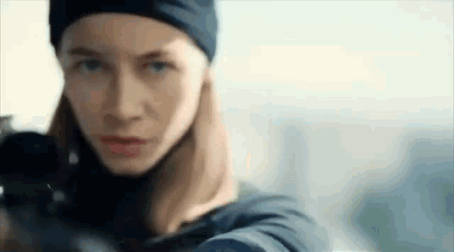 a woman in a black hat is holding a gun and pointing it at the camera .