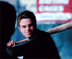 a man holds a baseball bat over his shoulder in front of a sign that says ' candy '