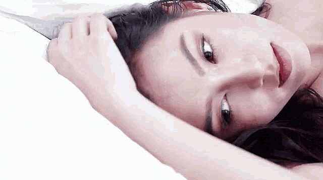a close up of a woman laying on a bed with her hand on her head