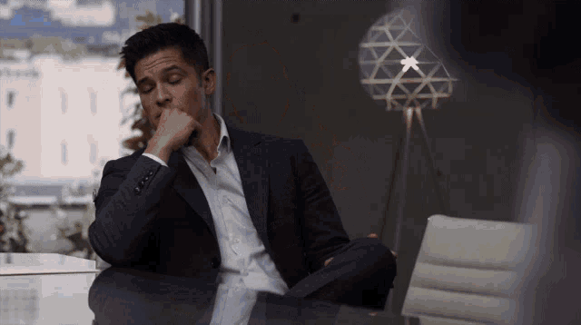 a man in a suit is sitting at a desk with his hand on his chin