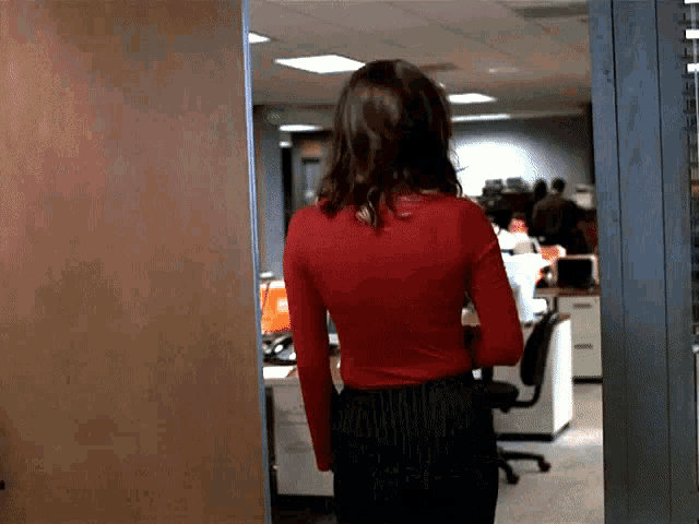 a woman in a red shirt is walking through an office door