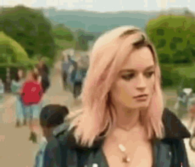 a woman with pink hair is wearing a black jacket and necklace .