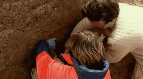a man in a red jacket is pointing at something in the dirt