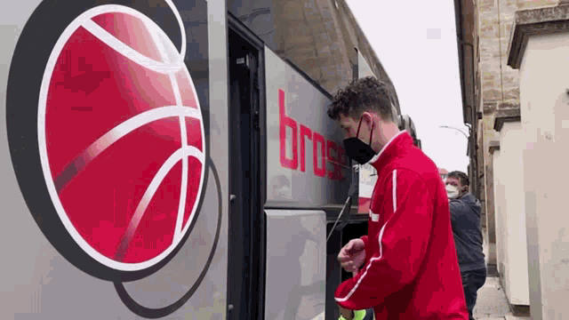 a man wearing a mask stands in front of a bus that says bros on it
