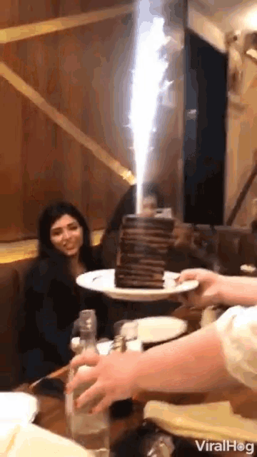 a woman sits at a table with a stack of pancakes on a plate with a firework coming out of it