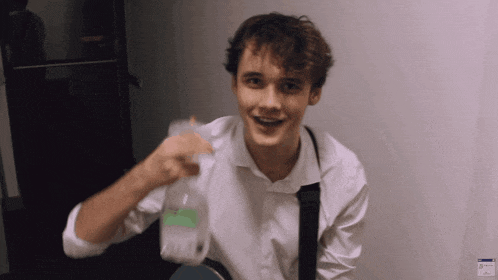 a young man in a white shirt and black tie holds a bottle