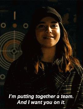 a woman wearing a hat and a plaid coat is smiling and saying `` i 'm putting together a team .
