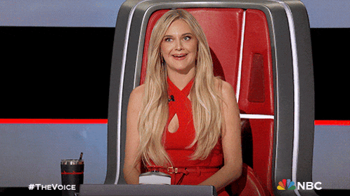 a woman in a red dress is sitting in a chair with a nbc logo on the bottom