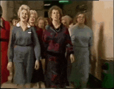 a group of women are walking down a hallway and singing together