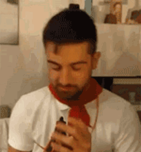 a man with a beard is wearing a red scarf around his neck while holding a cell phone .