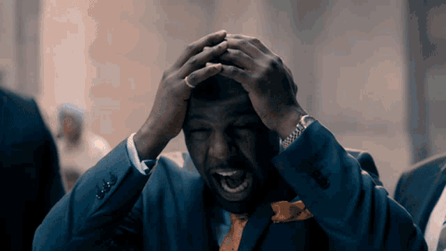 a man in a suit has his hands on his head and his mouth open