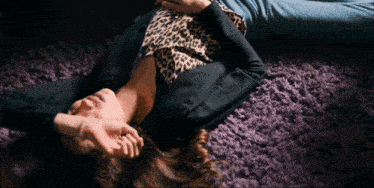 a woman wearing a leopard print top is laying on a purple rug