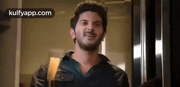 a man with a beard is standing in front of a glass door and smiling .