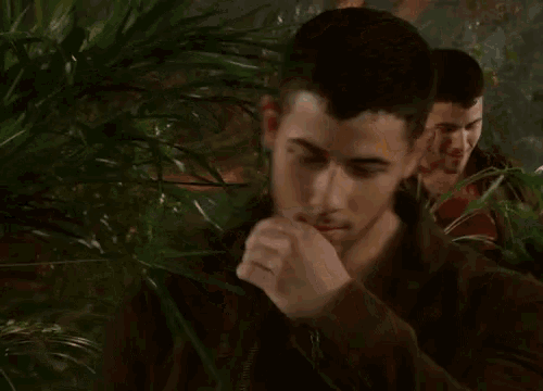 a man covering his mouth with his hand while another man holds a plant .