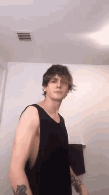 a man in a black tank top is standing in a bathroom .