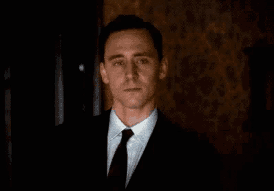 a man in a suit and tie is smiling while standing in a dark room .