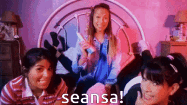 a group of girls are sitting on a bed and one of them is holding a wii remote
