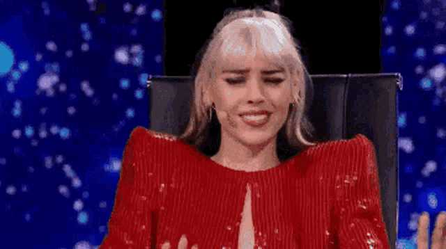 a woman in a red dress is sitting in a chair and making a face .