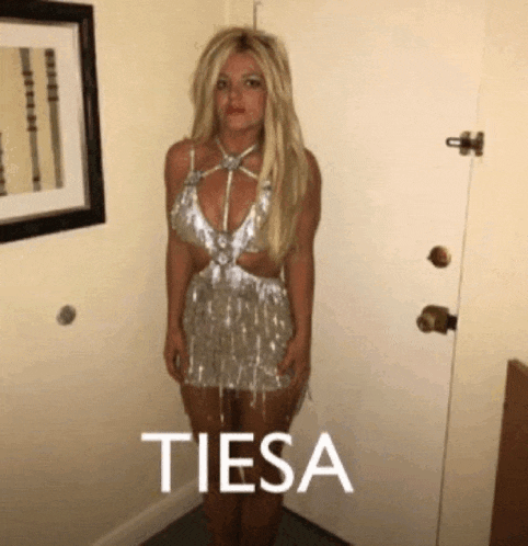 a woman in a silver dress is standing next to a door with the word tiesa written on it