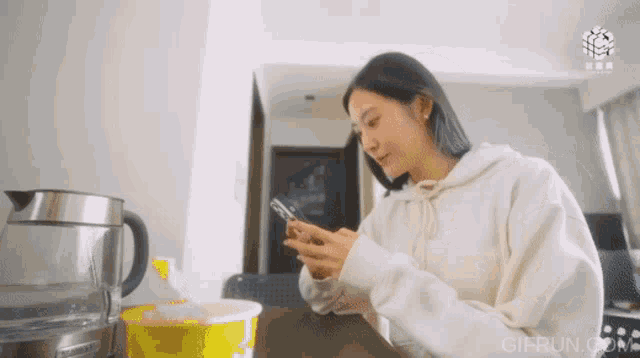 a woman in a white sweatshirt is looking at her phone