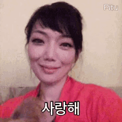 a woman in a red shirt is smiling and holding a cat in her arms .