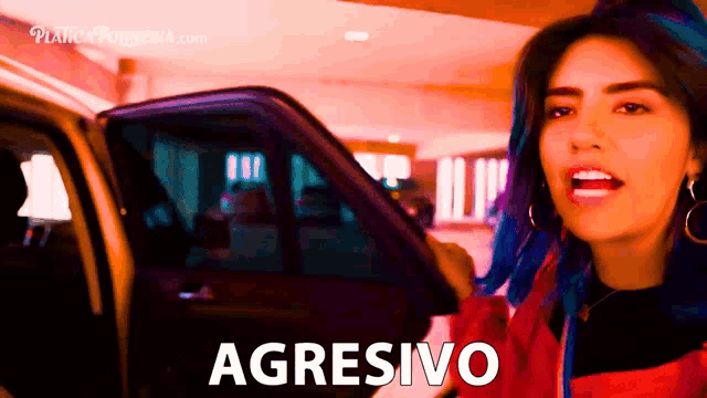 a woman with blue hair is standing in front of a car with the word agresivo written on the door