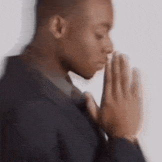 a man in a suit is praying with his hands folded in front of his face .